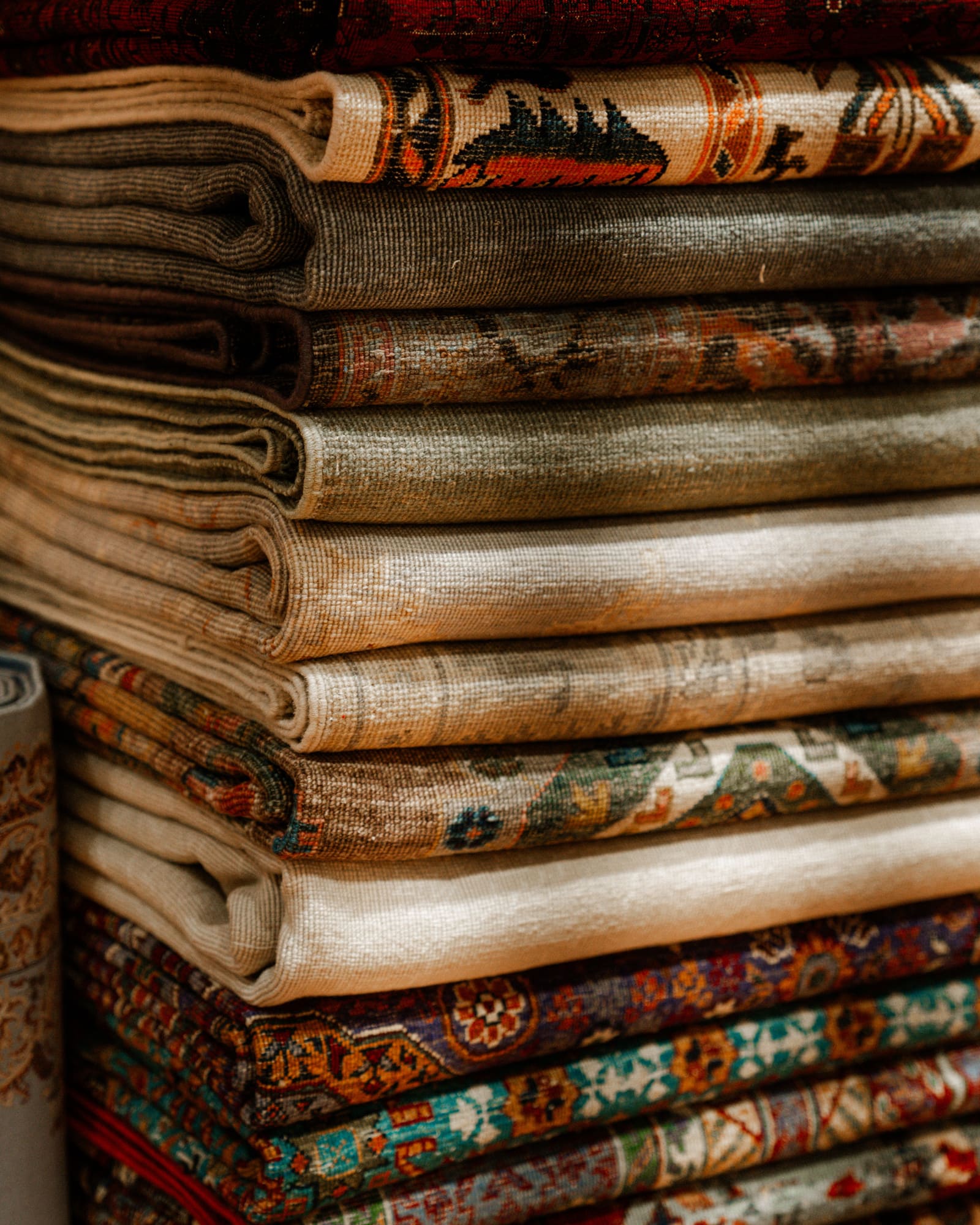 A stack of folded patterned rugs in deep reds, creams and muted greens