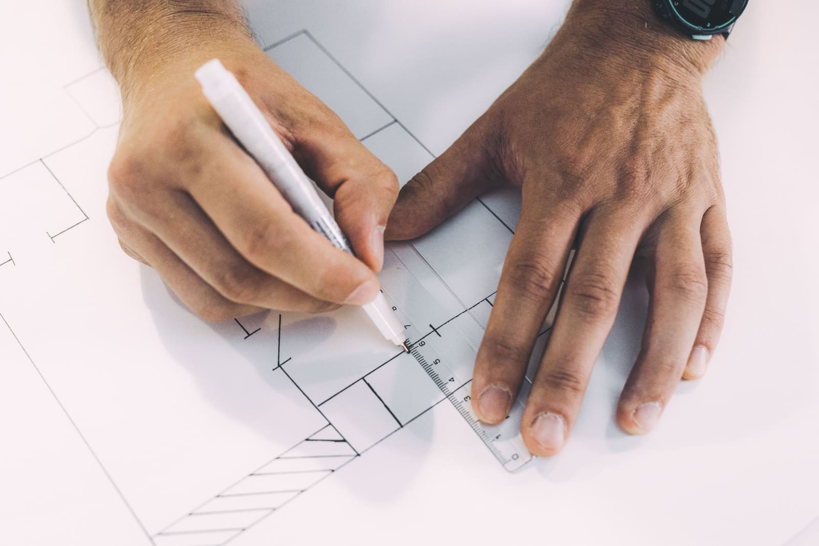 Hands drawing a floor plan with a pen and a clear ruler