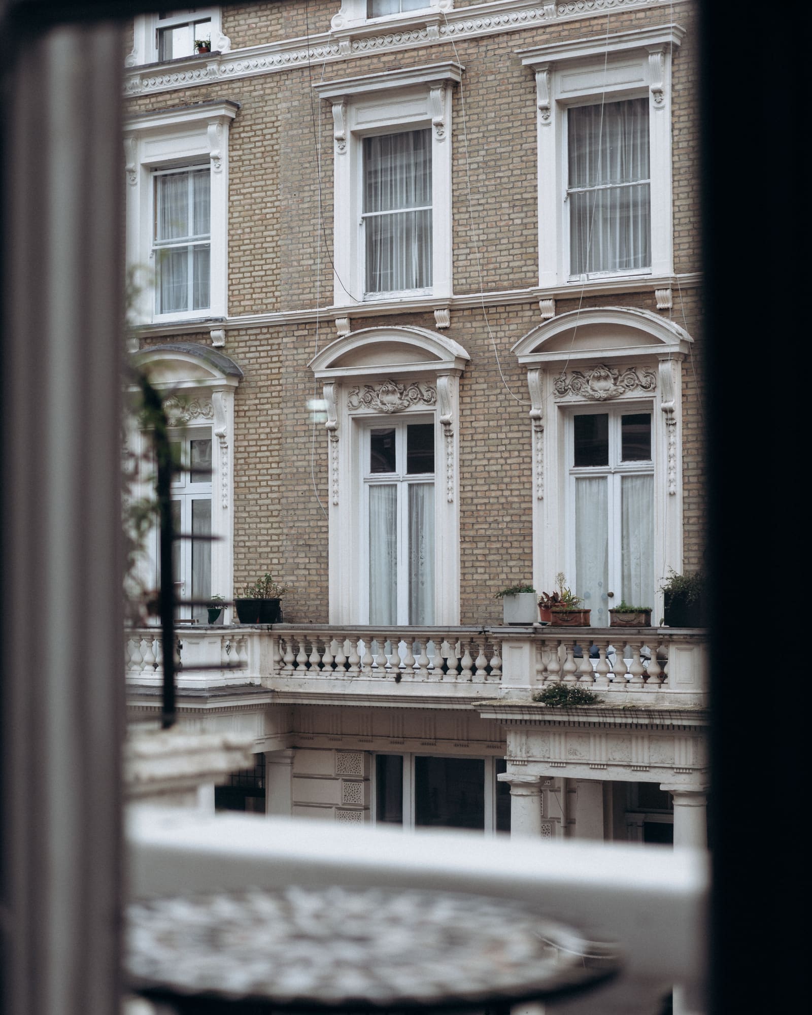A pale brick and white stucco terrace with a balustraded balcony, seen through a window
